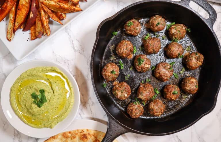 Cilantro Jalapeno Hummus in a bowl with lamb kofta in a cast iron skillet sweet potato fries shown in top left corner