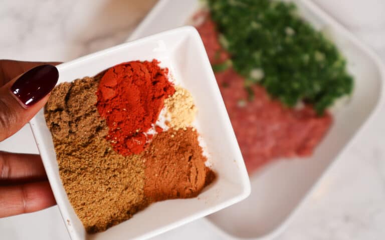 close up of seasoning mixture in a ramekin with ground lamb in a bowl with parley in the background