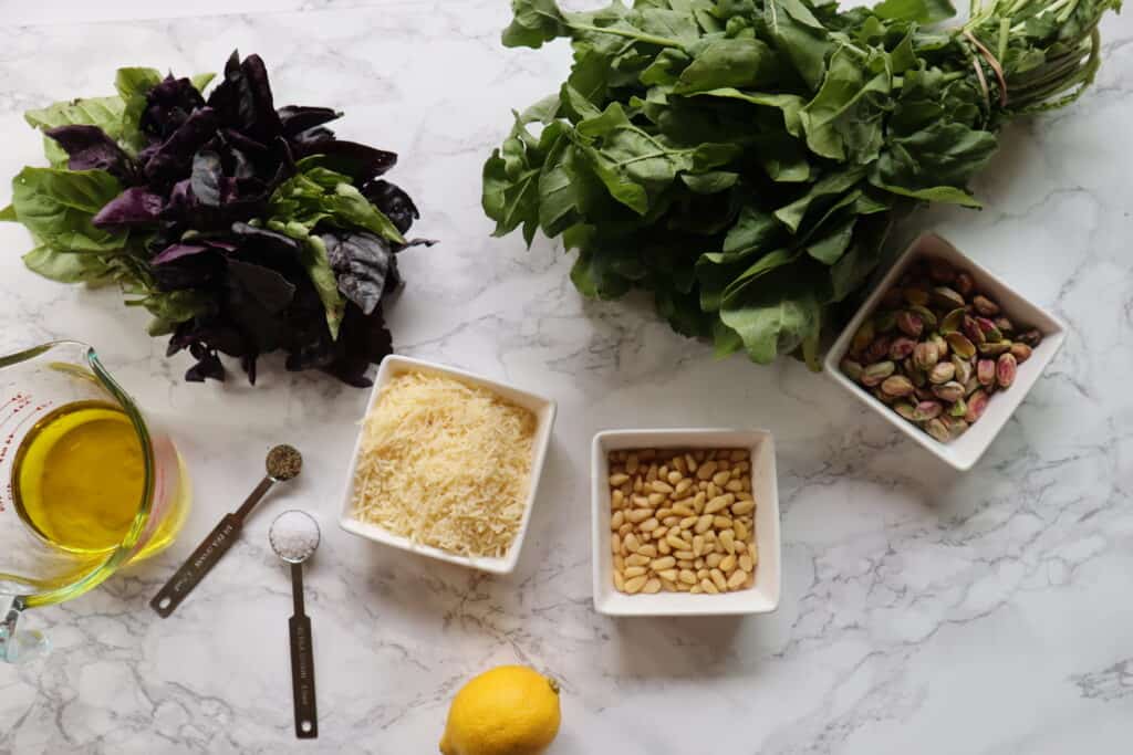 pistachio pesto ingredients shown are olive oil spices parmesan cheese pine nuts lemon pistachios arugula and basil