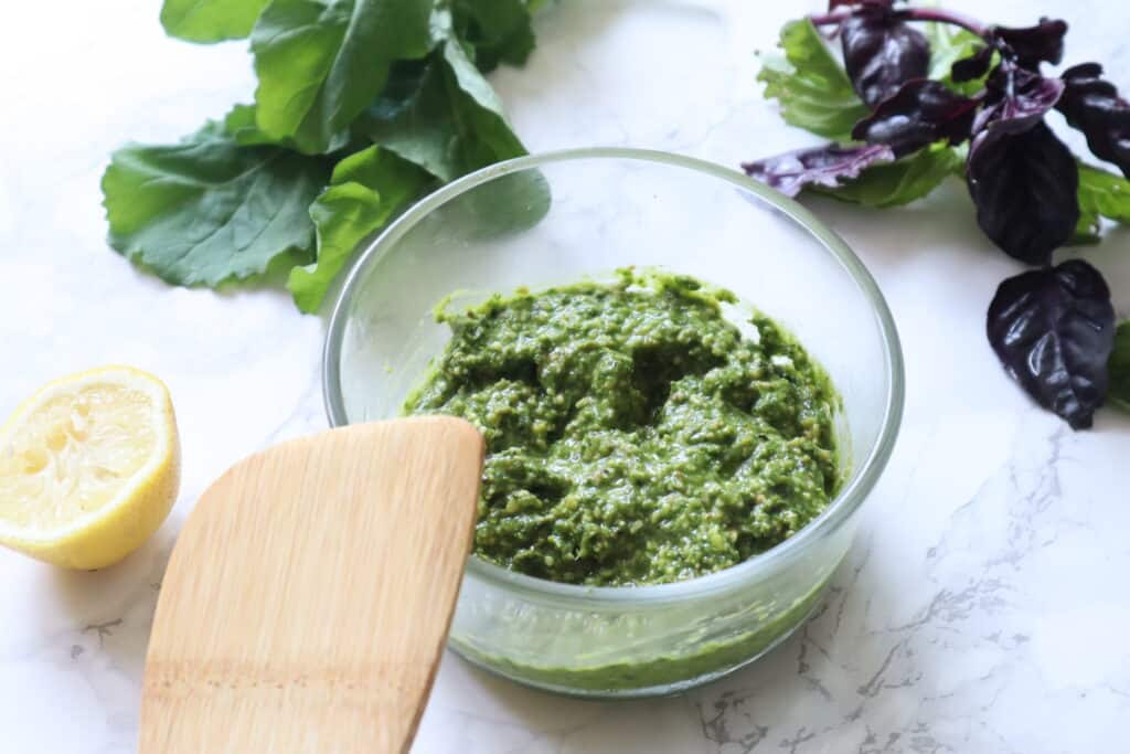 bowl of pistachio pesto with basil and lemon in the background and wooden spoon on the bowl