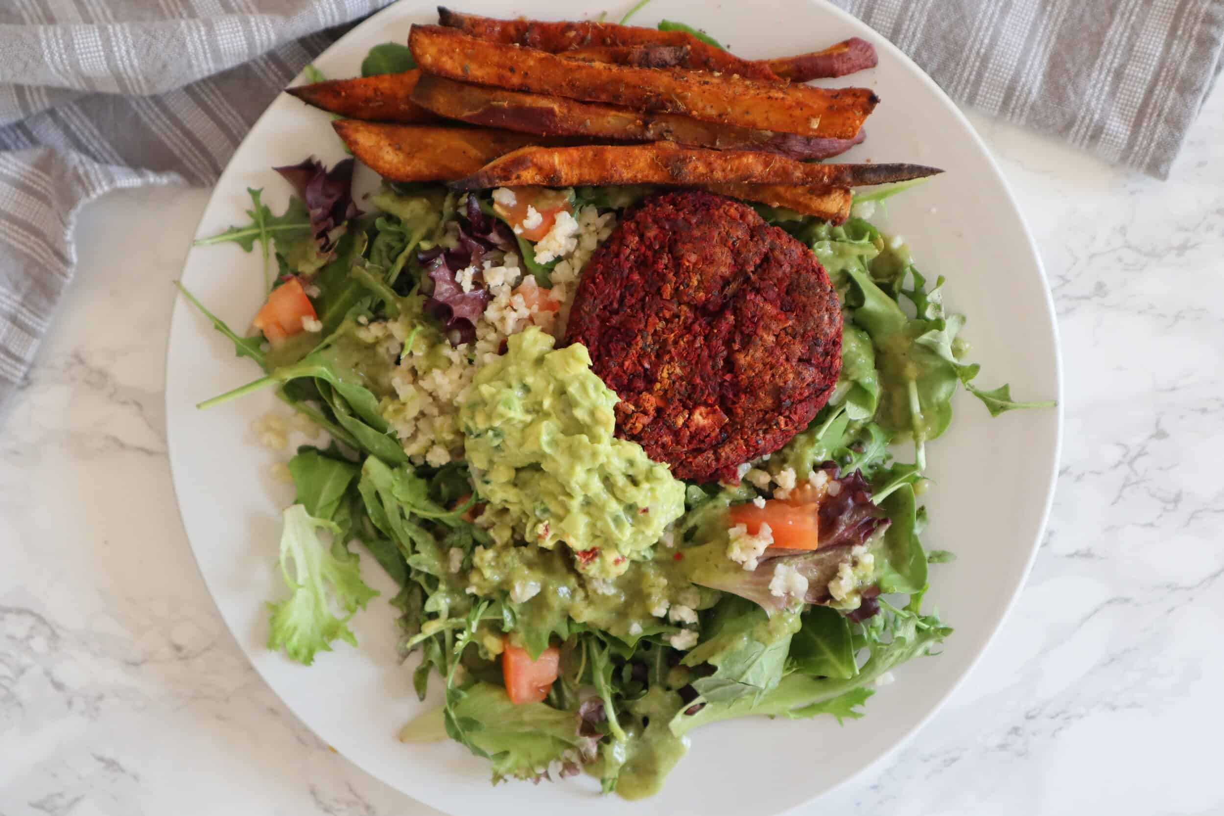 plate of salad topped with beet burger sweet potato fries and guacamole