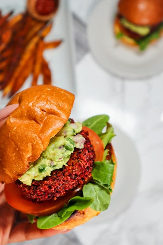 quinoa beet burger with guac tomato and arugula with plate of fries in the background