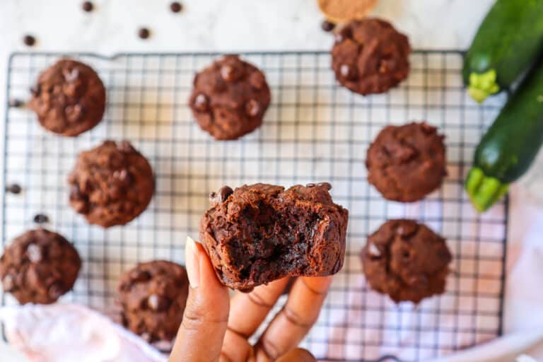 A hand holding a moist chocolate zucchini muffin with a gooey center.