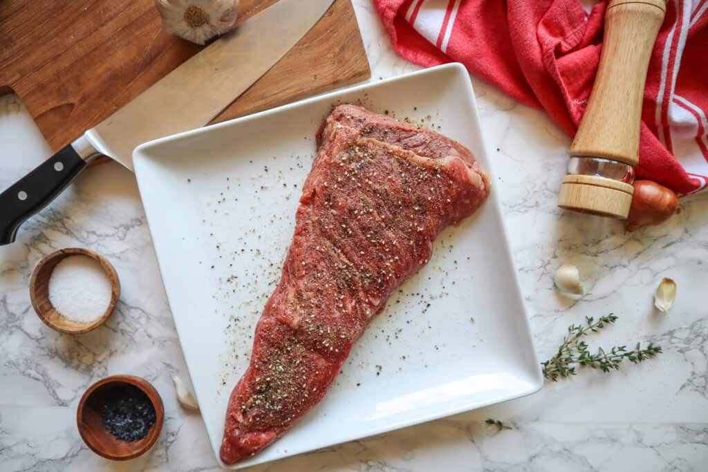Plated raw tri-tip steak seasoned with salt, pepper and garlic.
