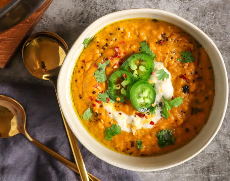 bowl of carrot lentil soup topped with jalapenos, dairy free yogurt, and cilantro