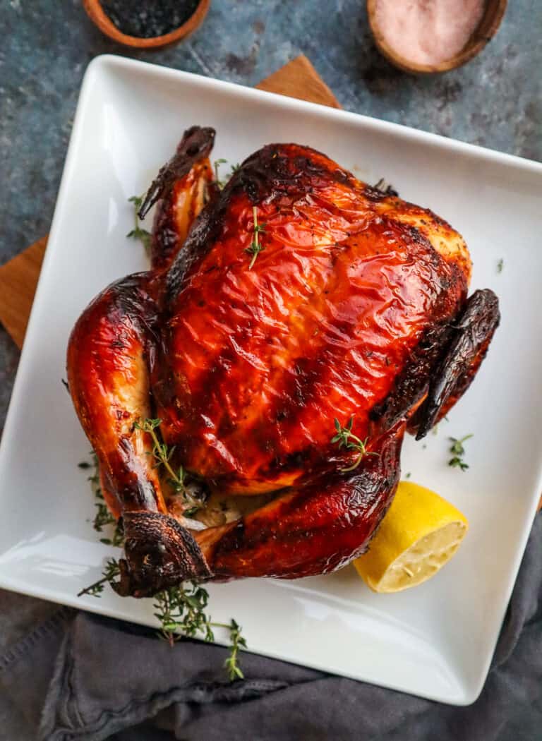 fully cooked buttermilk brined chicken on a white plate with thyme and a half lemon wedge