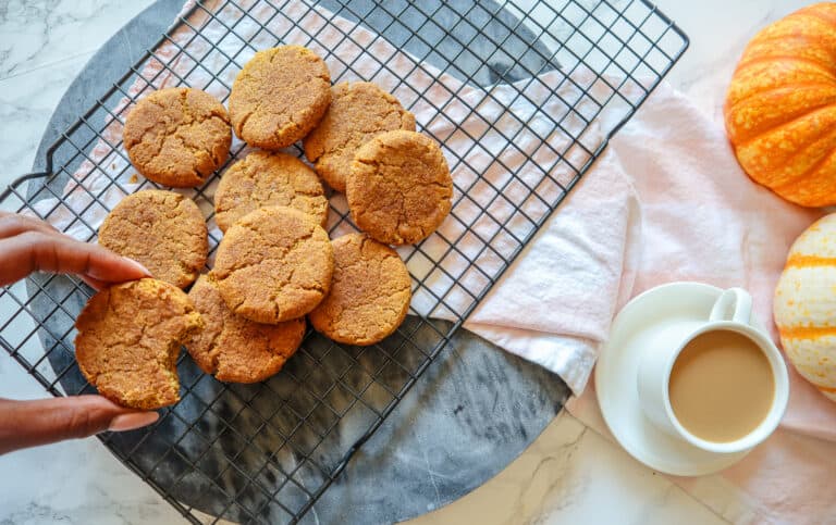 pumpkin snickerdoodles on a wire rack after baking with one being held by hand over the cookies
