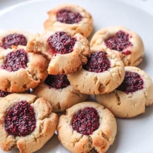 plate of twelve jam filled thumbprint cookies stacked on a white plate