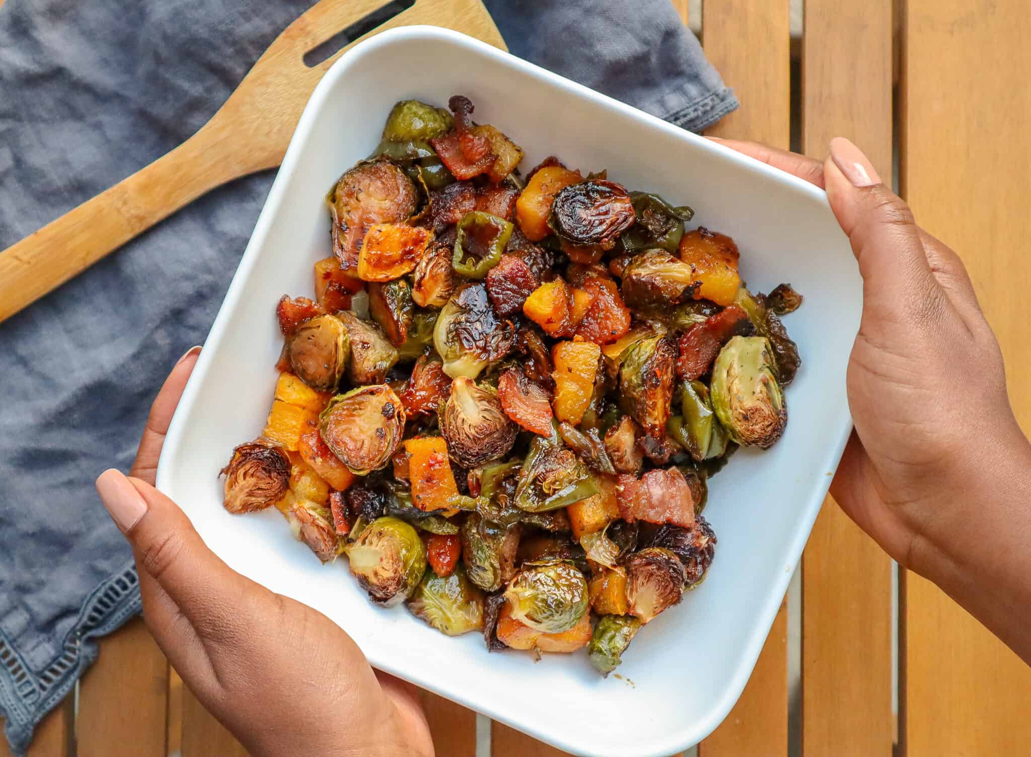 hands holding bowl of maple roasted brussels sprouts with bacon and butternut squash