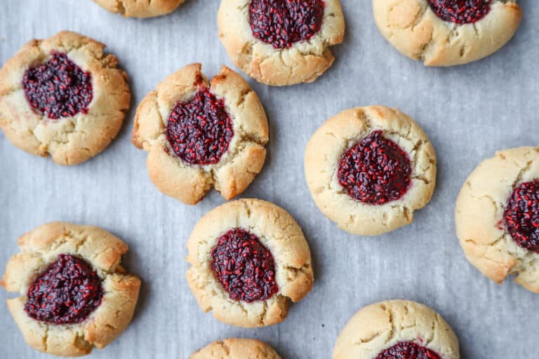 close up of raspberry jam filled thumbprint cookies on parchment paper