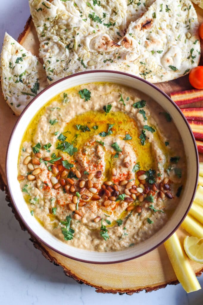 Baba ganoush recipe, close up of finished baba ganoush topped with pine nuts, parsley, olive oil, and served with pita bread, tomatoes, and carrots