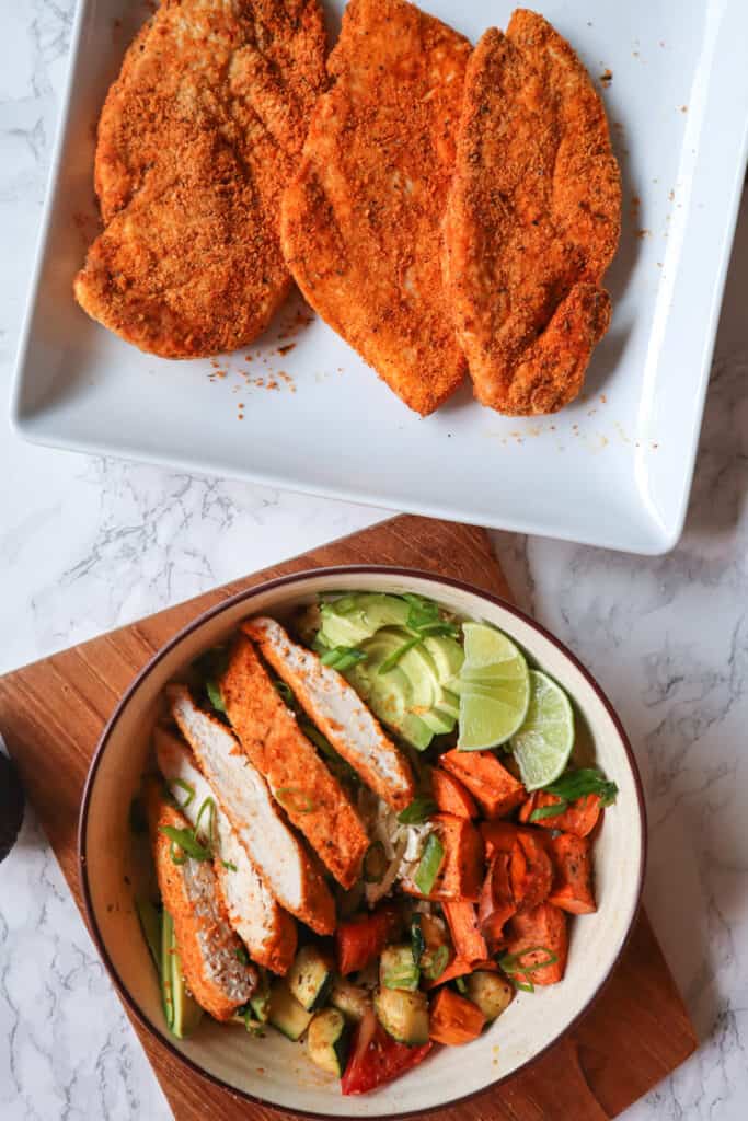 3 Crispy gluten free air fryer chicken breasts on a plate and a bowl of sliced chicken breast with rice, vegetables, lime, and avocado
