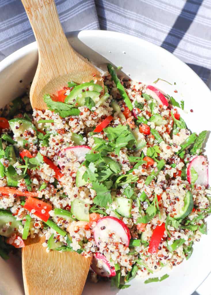 Quinoa Vegetable Salad in a large white bowl with two wooden spoons in the bowl