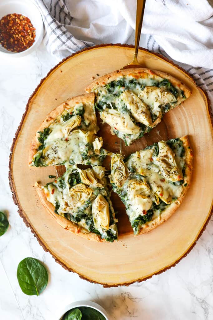 over head image of spinach artichoke pizza cut into four slices