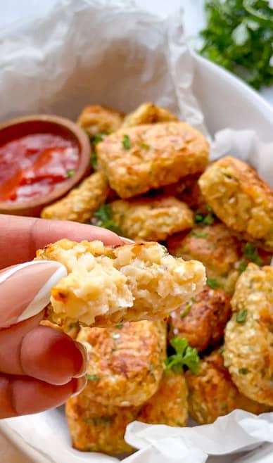 close up of cauliflower tater tots being held with a bowl of tots in the background