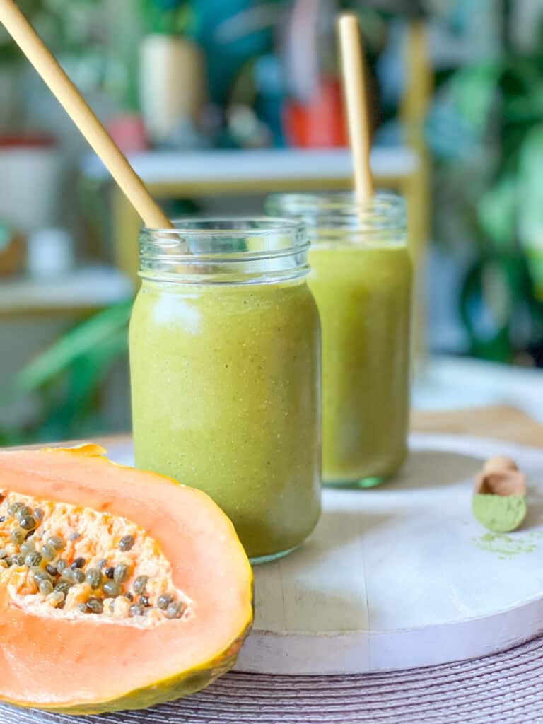 Two Moringa Papaya Smoothies with papaya fruit in photo next to the smoothie