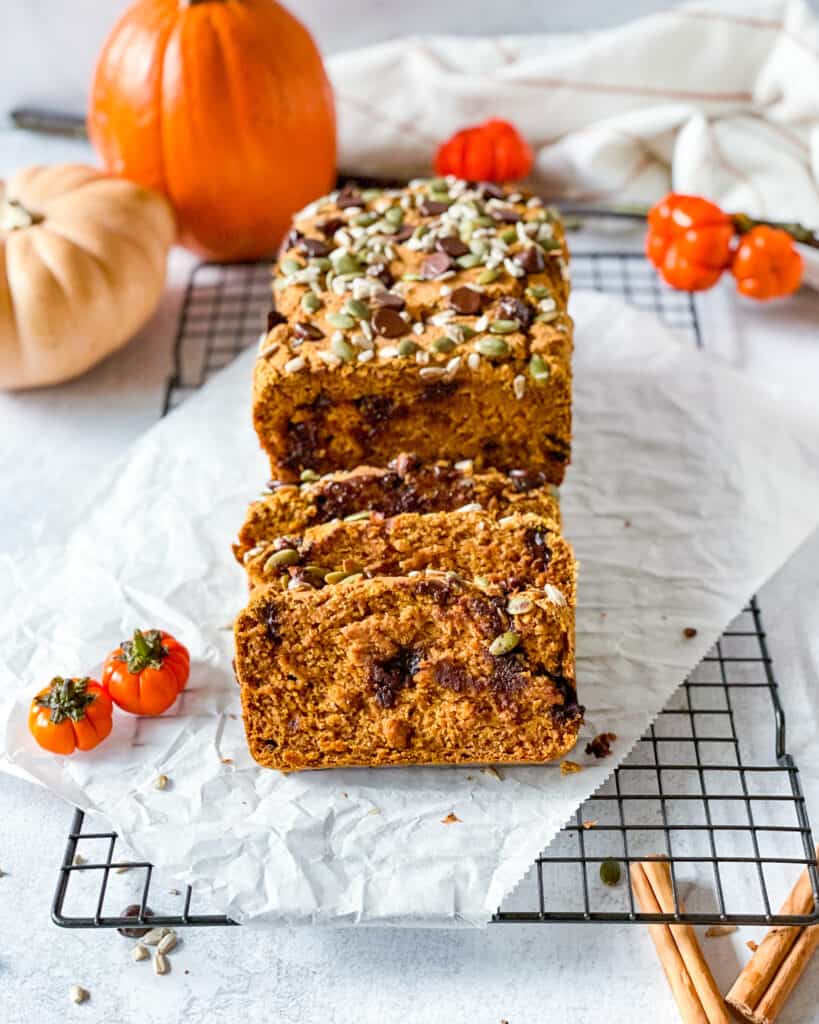 sliced chocolate chip pumpkin bread on a wire rack and parchment paper small and large pumpkins are placed in the photo for decoration
