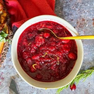 bowl of orange cranberry sauce with gold spoon. red cloth in background in top left corner