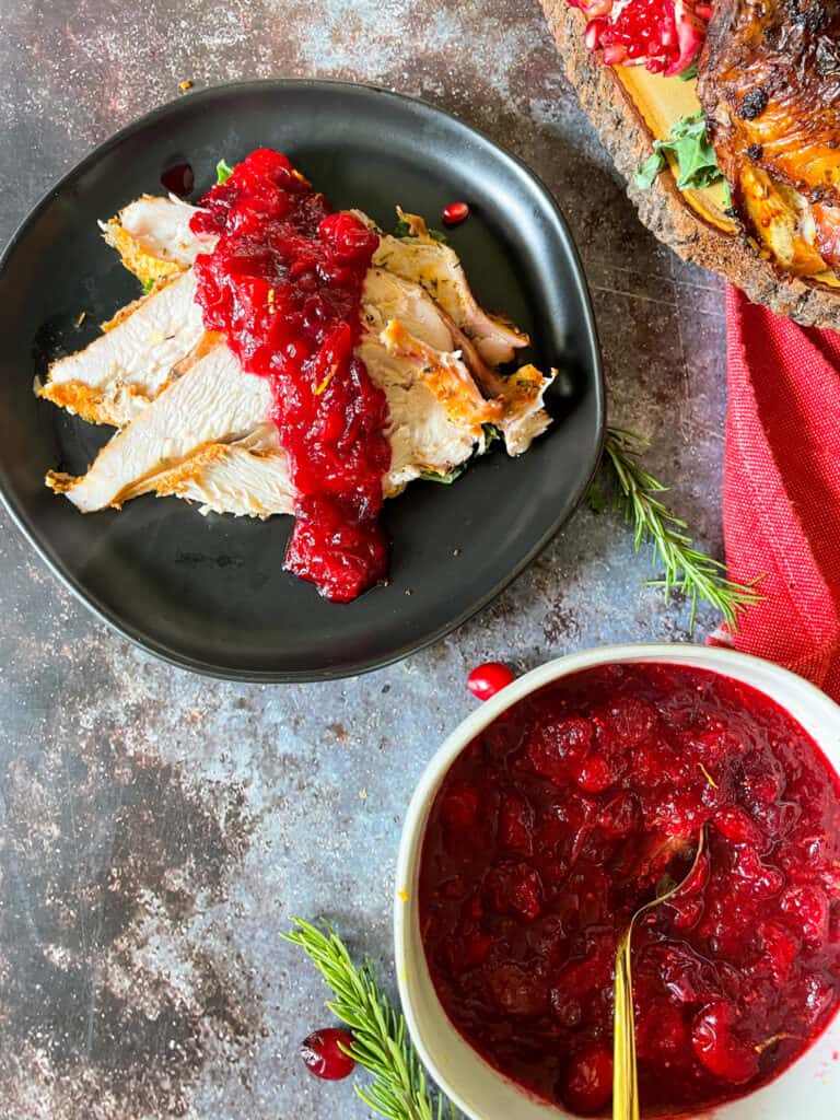 sliced turkey breast with orange cranberry sauce on top. bowl of homemade orange cranberry sauce in the bottom right corner