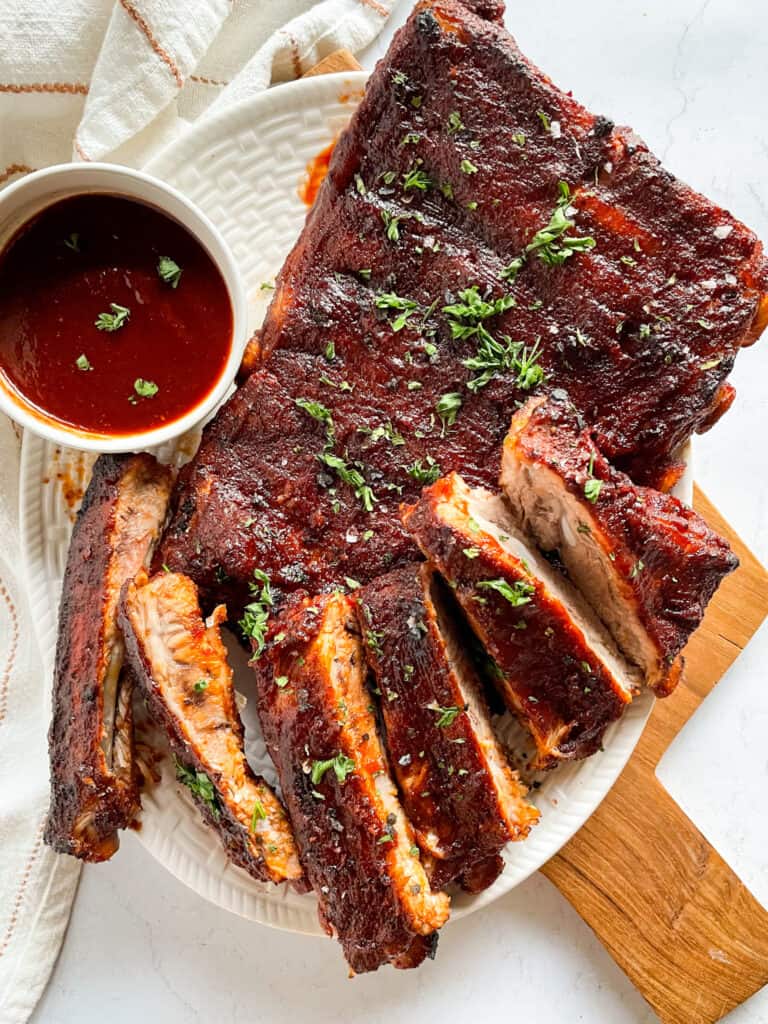 Plated Instant Pot Ribs coated in barbecue sauce with a small bowl of barbecue sauce to the left.