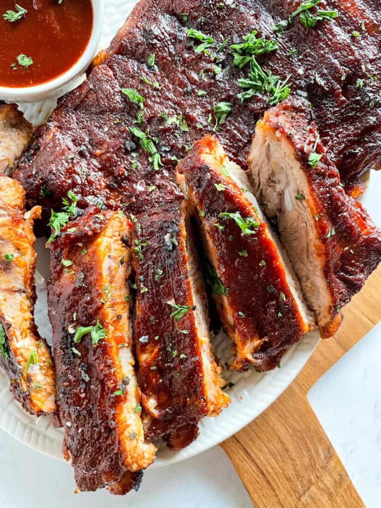 A close up view of Instant Pot Ribs with a small bowl of homemade barbecue sauce in the upper left corner.