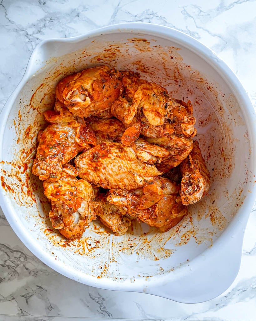 air fryer chicken wings with spices in a large white bowl before cooking