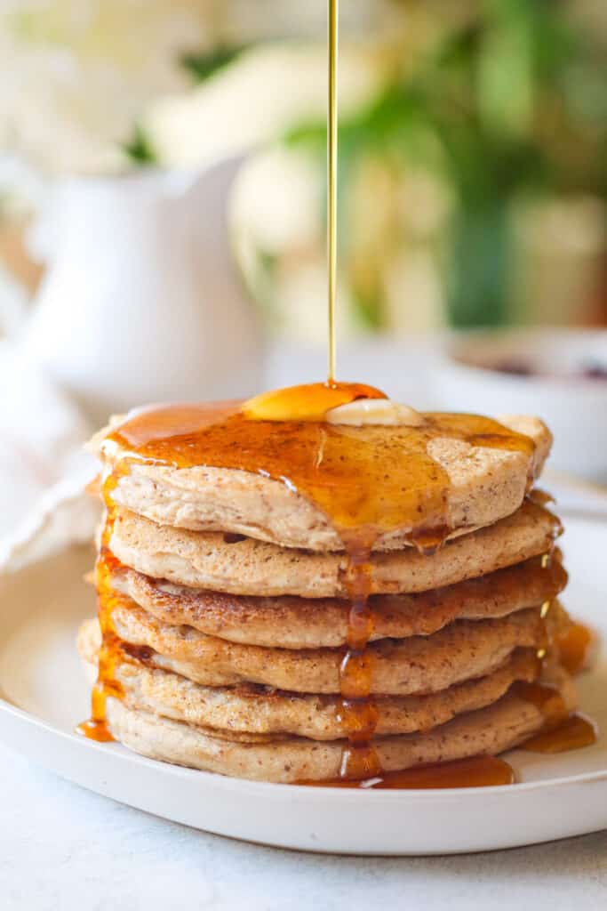 vegan gluten free pancakes stacked with maple syrup drizzled on the pancake