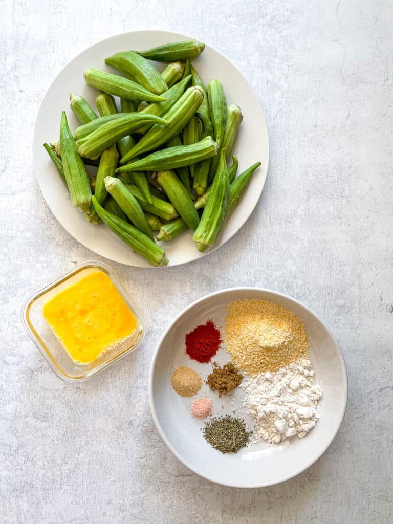plate of okra, small bowl of beaten egg, large bowl with cornmeal, flour, and seasonings
