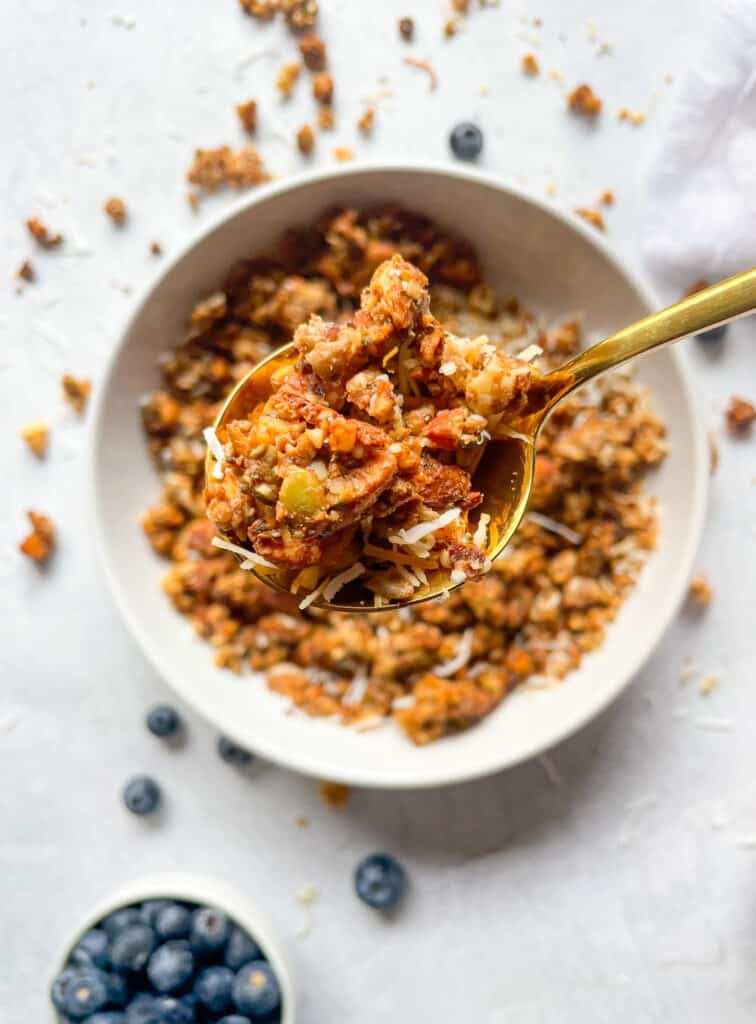 Date Sweetened Grainless Granola, close up on a spoon to show texture with granola in a bowl in the background