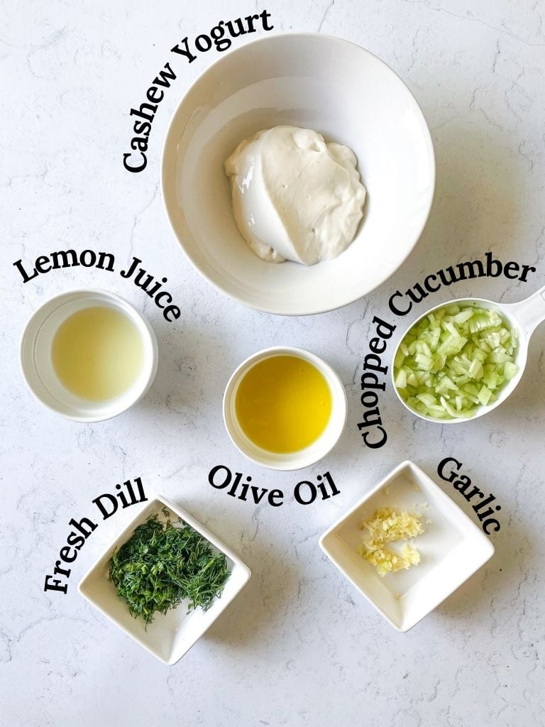 ingredients to make vegan tzatziki, cashew yogurt, lemon juice, olive oil, chopped cucumber, fresh dill, minced garlic