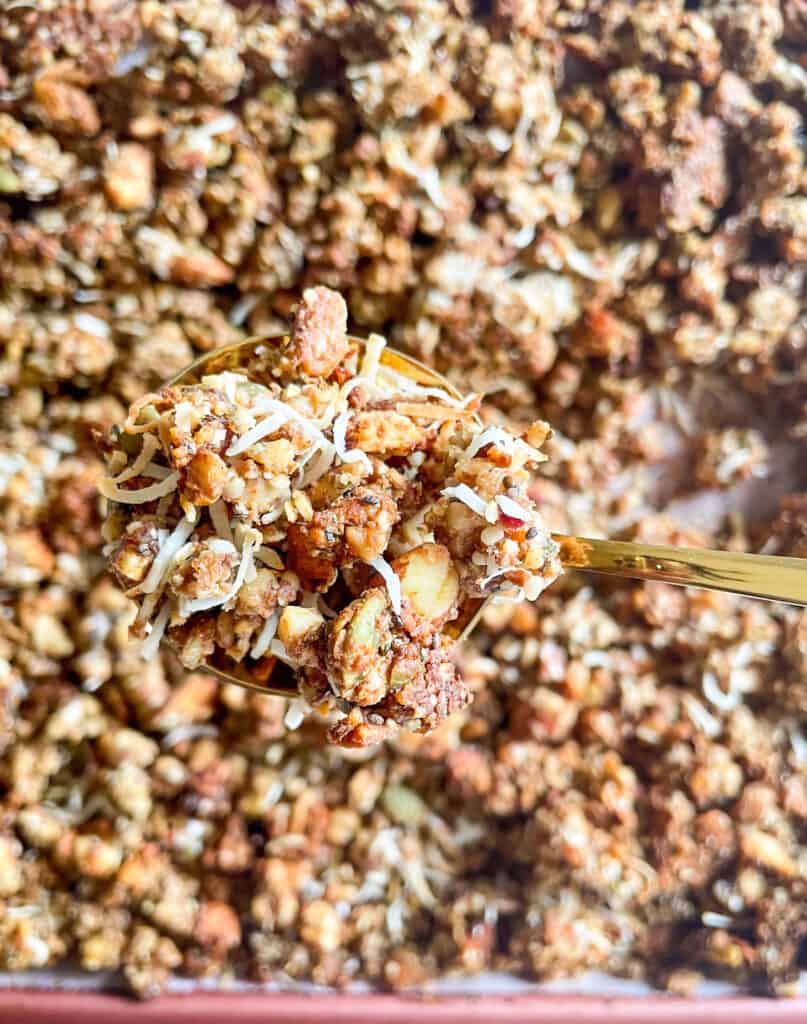 close up of grain-free granola on a spoon to show texture with sheet tray of granola in he background