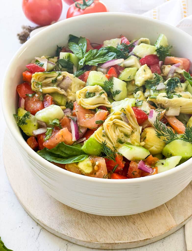 healthy salad made with cucumbers, tomatoes, basil, dill, vinegar, artichoke, avocado, and fresh herbs