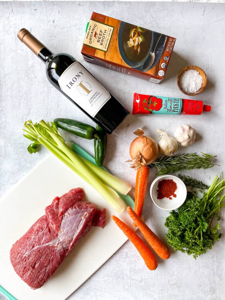 ingredients needed to make red wine-braised beef brisket: celery, carrots, onion, garlic, fresh herbs, tomato paste, wine, beef broth, wine