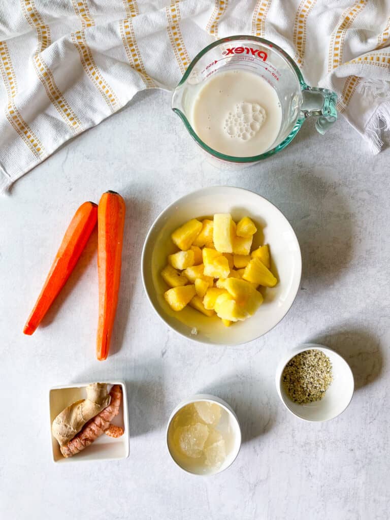ingredients needed to make a carrot smoothie: non-dairy milk, frozen pineapple, carrots, turmeric, ginger, sea moss gel, hemp seeds, pineapple
