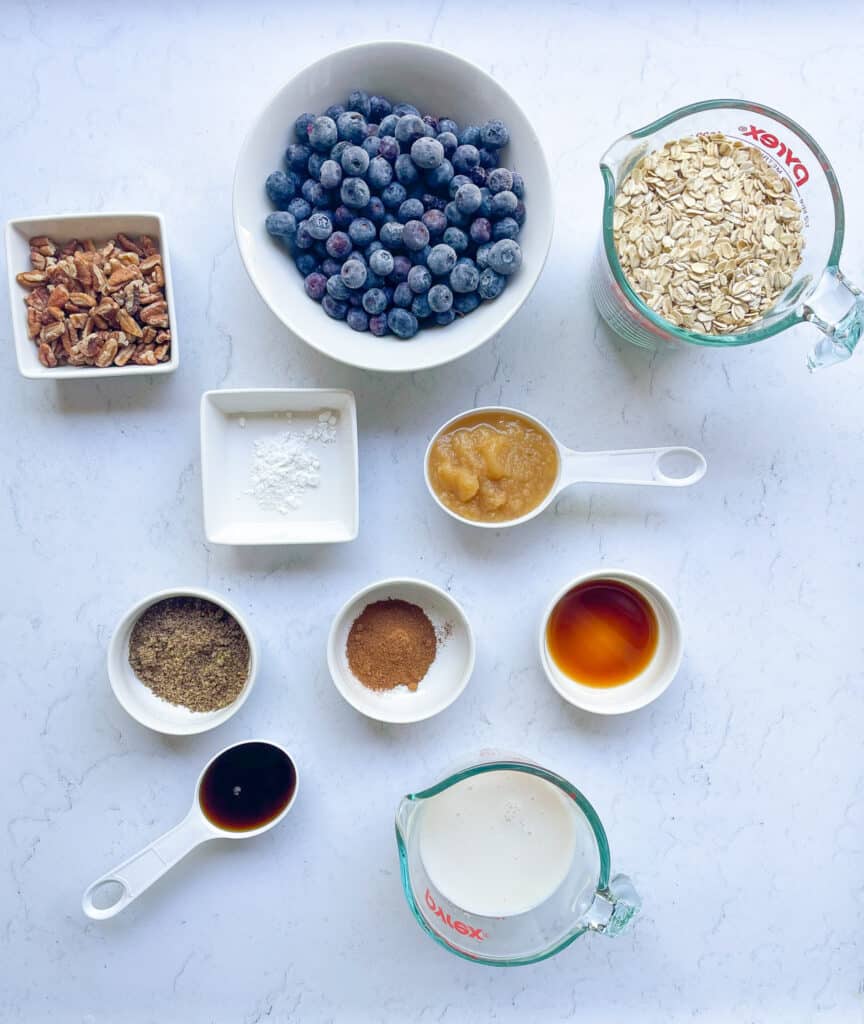 ingredients needed to make the best blueberry baked oatmeal: blueberries, gluten free rolled oats, flax seeds, pecans, baking powder, cinnamon, vanilla, maple syrup, non-dairy milk, and applesauce