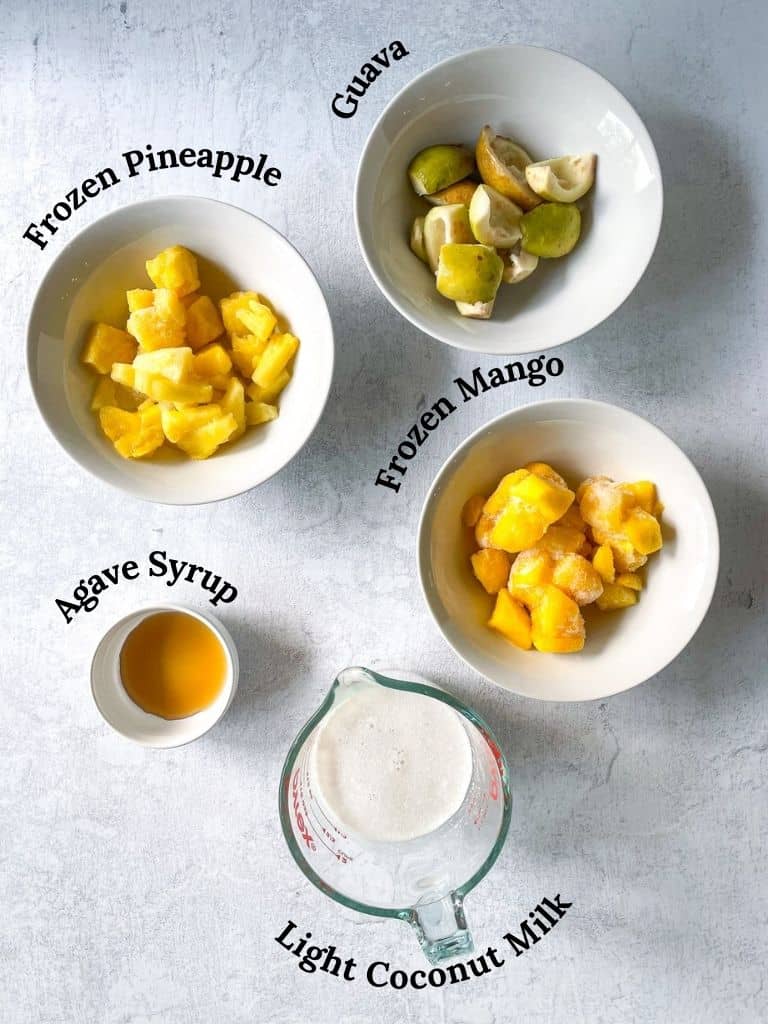 Ingredients needed to make a tropical guava smoothie: mango, pineapple, guave, agave, coconut milk shown