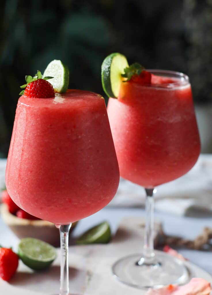 two glasses of frozen rose, wine slushies (frose) garnished with strawberries and lime