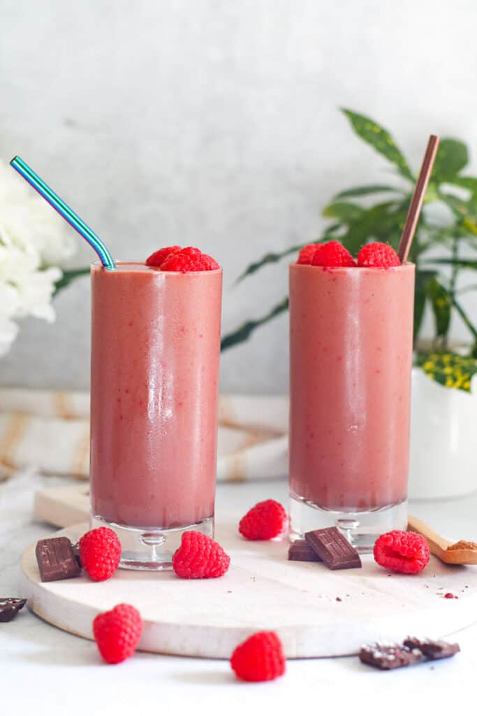 two chocolate raspberry sea moss smoothies in a tall glass topped with raspberries