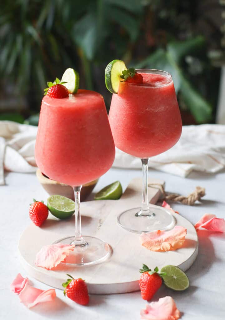 two glasses of frozen rose, wine slushies (frose) decorated with strawberries and lime