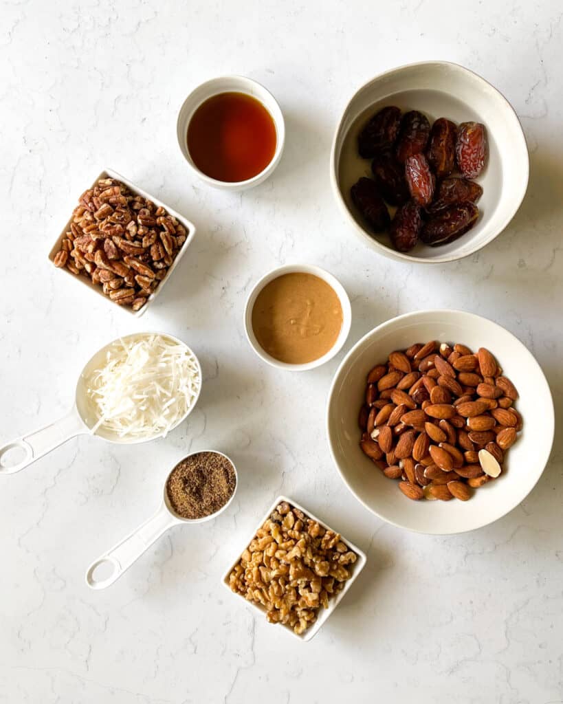 ingredients shown to make grain free peanut butter granola bars: medjool dates, chopped pecans, roasted almonds, walnuts, flaxseeds, shredded coconut, maple syrup