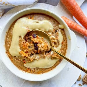 A bowl of carrot cake baked oats with a spoon in the middle, revealing the interior of the cake