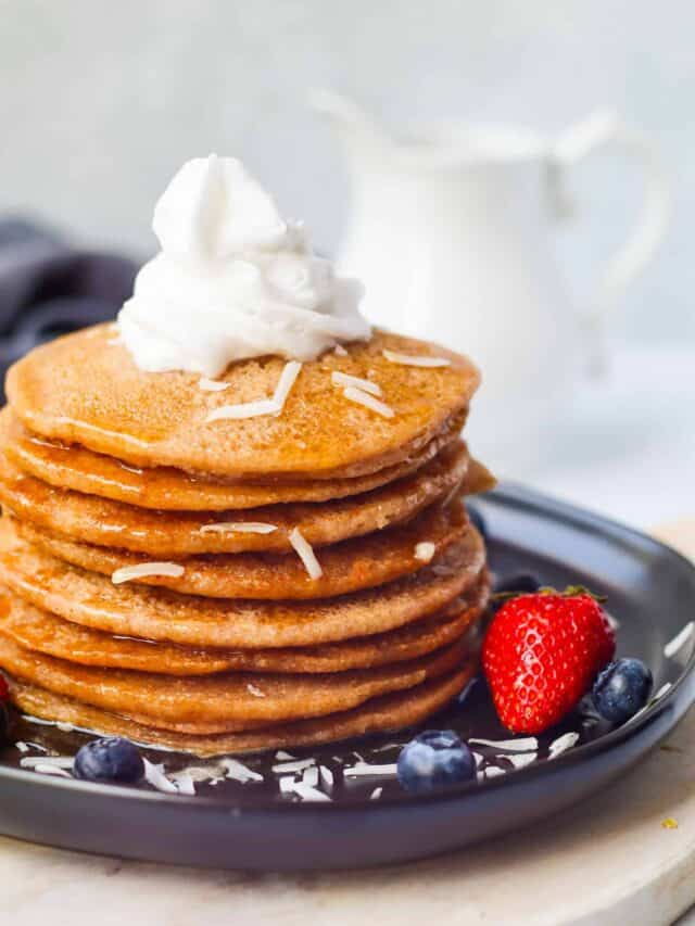 stack of vegan buckwheat pancakes with coconut whipped cream and blueberries and strawberries on the plate