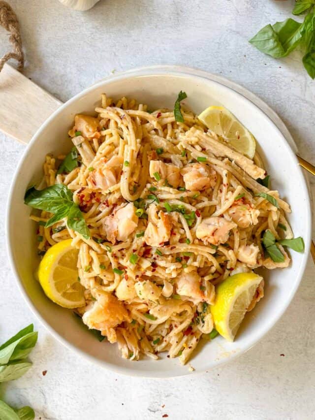 creamy lobster pasta in a white bowl with lemons and fresh basil