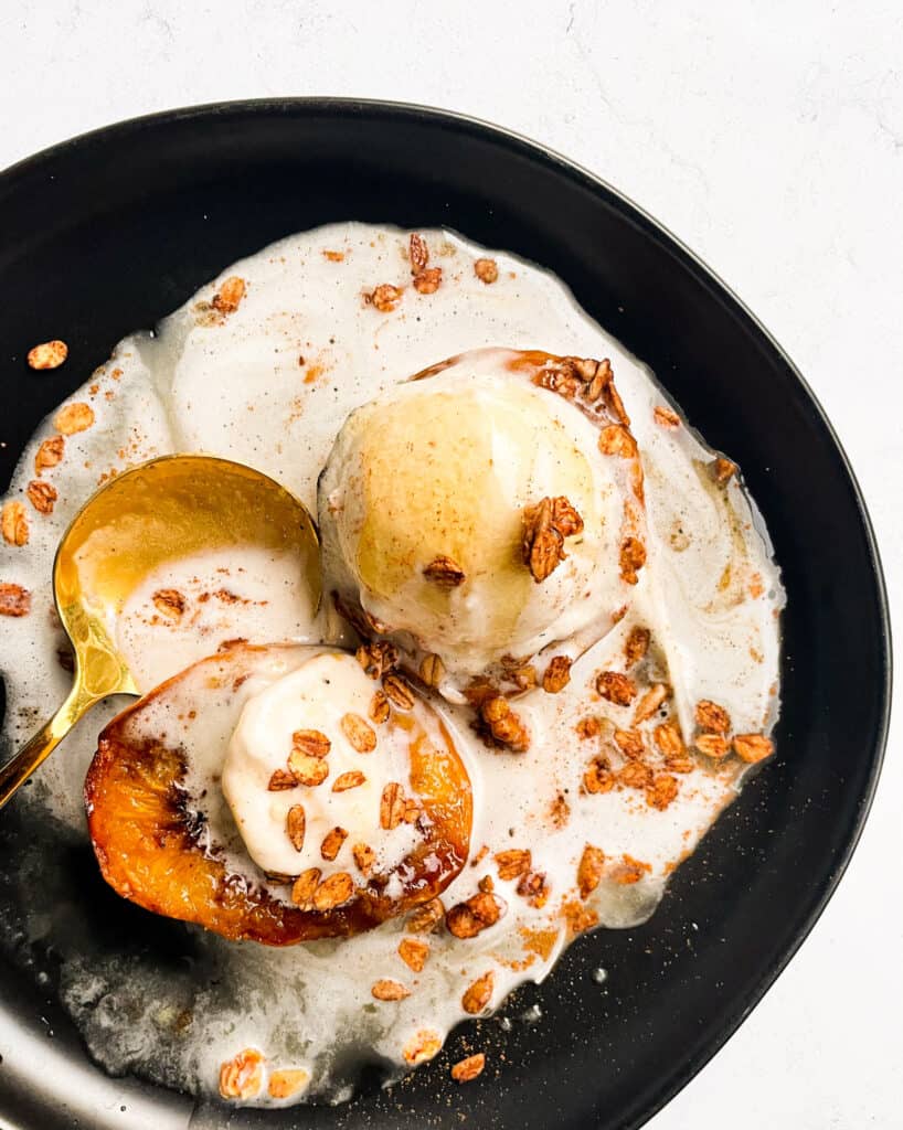 a plate of 2 peach halves made in the air fryer topped with vanilla ice cream, granola oats, and honey. served with a gold spoon