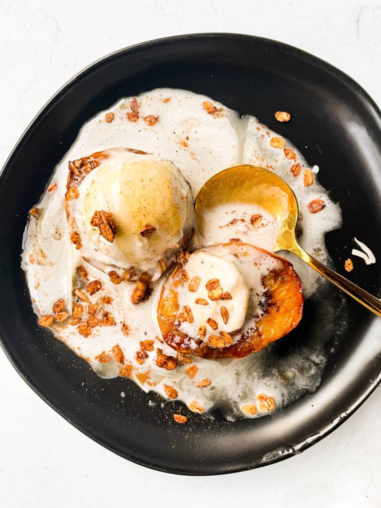 a plate of 2 peach halves made in the air fryer topped with vanilla ice cream, granola oats, and honey. served with a gold spoon