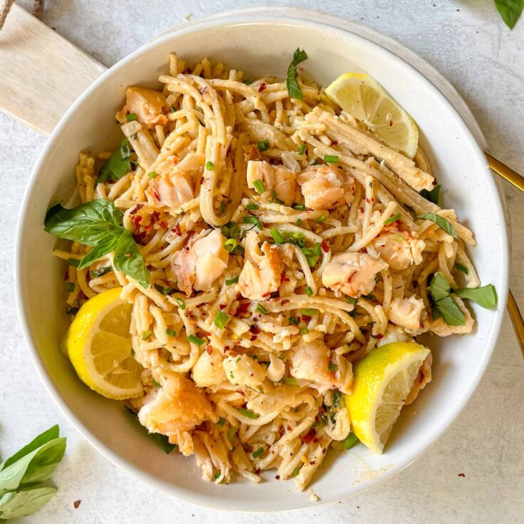 overhead view of a bowl of creamy lobster pasta with sliced lemon for garnish