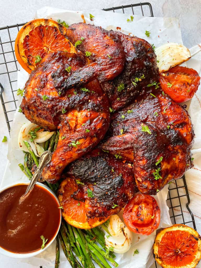 Grilled Butterfly bbq chicken with a side of barbecue sauce and grilled vegetables