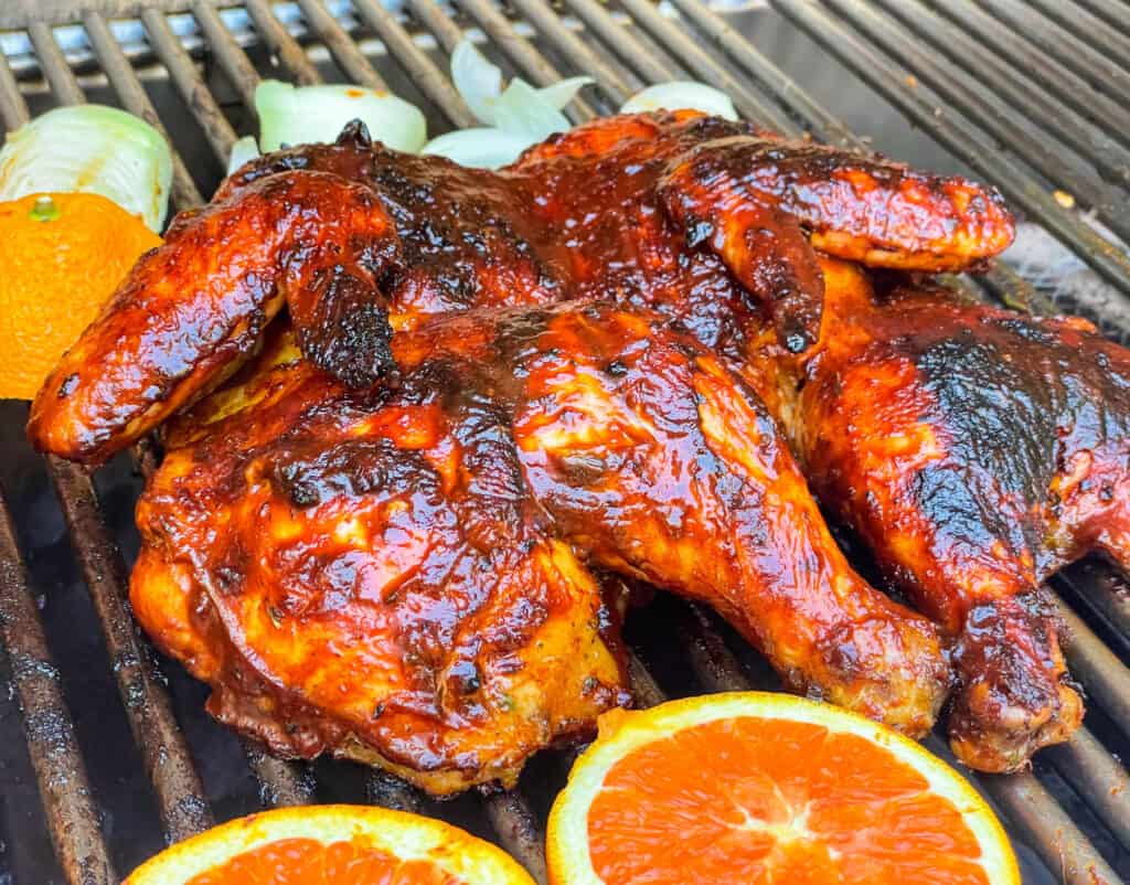 spatchcock chicken on the grill alongside orange slices and onions