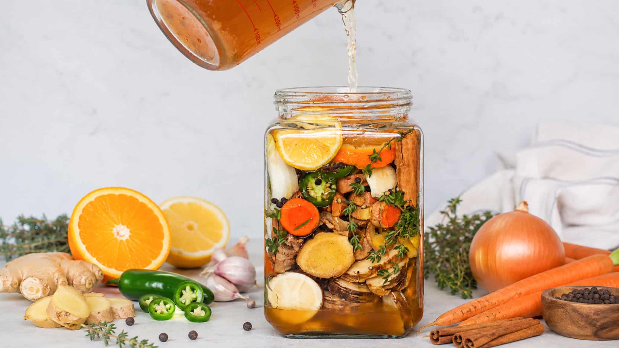 pouring apple cider vinegar into large glass jar mixed with fire cider ingredients