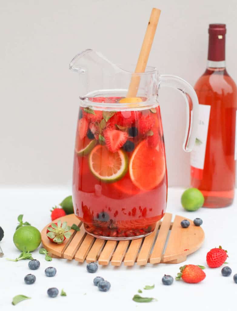 a large pitcher of rose sangria with fresh fruit with bottle or rose in the background